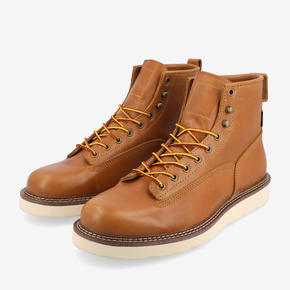 A pair of tan leather work boots with yellow laces and white rubber soles.