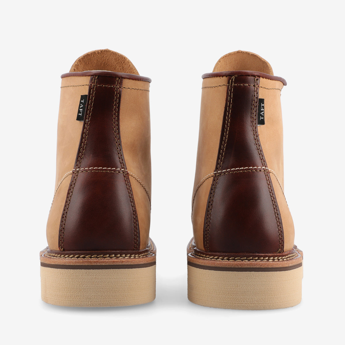 Rear view of a pair of tan leather boots with dark brown accents, showcasing detailed stitching and sturdy soles against a white background.