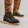 Close-up of a person wearing brown corduroy pants and dark leather lace-up boots with beige soles, standing on a light-colored floor.