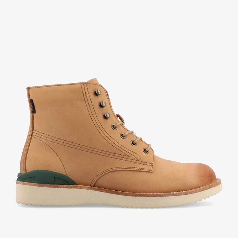 A tan leather boot with green detail on the heel, white sole, and metal eyelets for laces, viewed from the side.