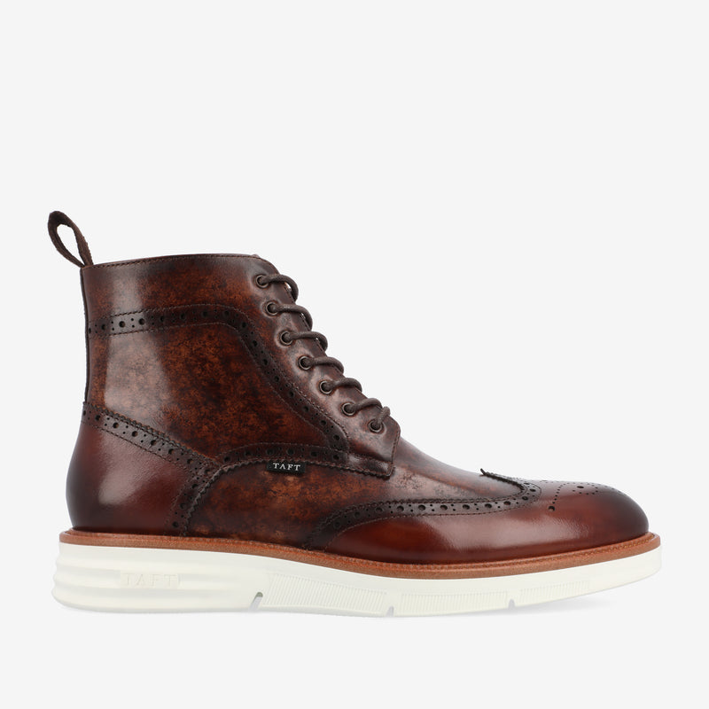 A brown leather brogue boot with white rubber sole, featuring a lace-up design, wingtip detailing, and a pull tab at the back.