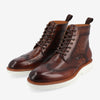 Brown leather Brogue boots with white soles, featuring detailed brogue patterning, ankle height, and pull tabs at the back.