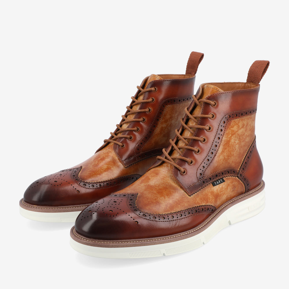 A pair of two-tone brown leather wingtip boots with white soles, decorative broguing, and lace-up fronts.