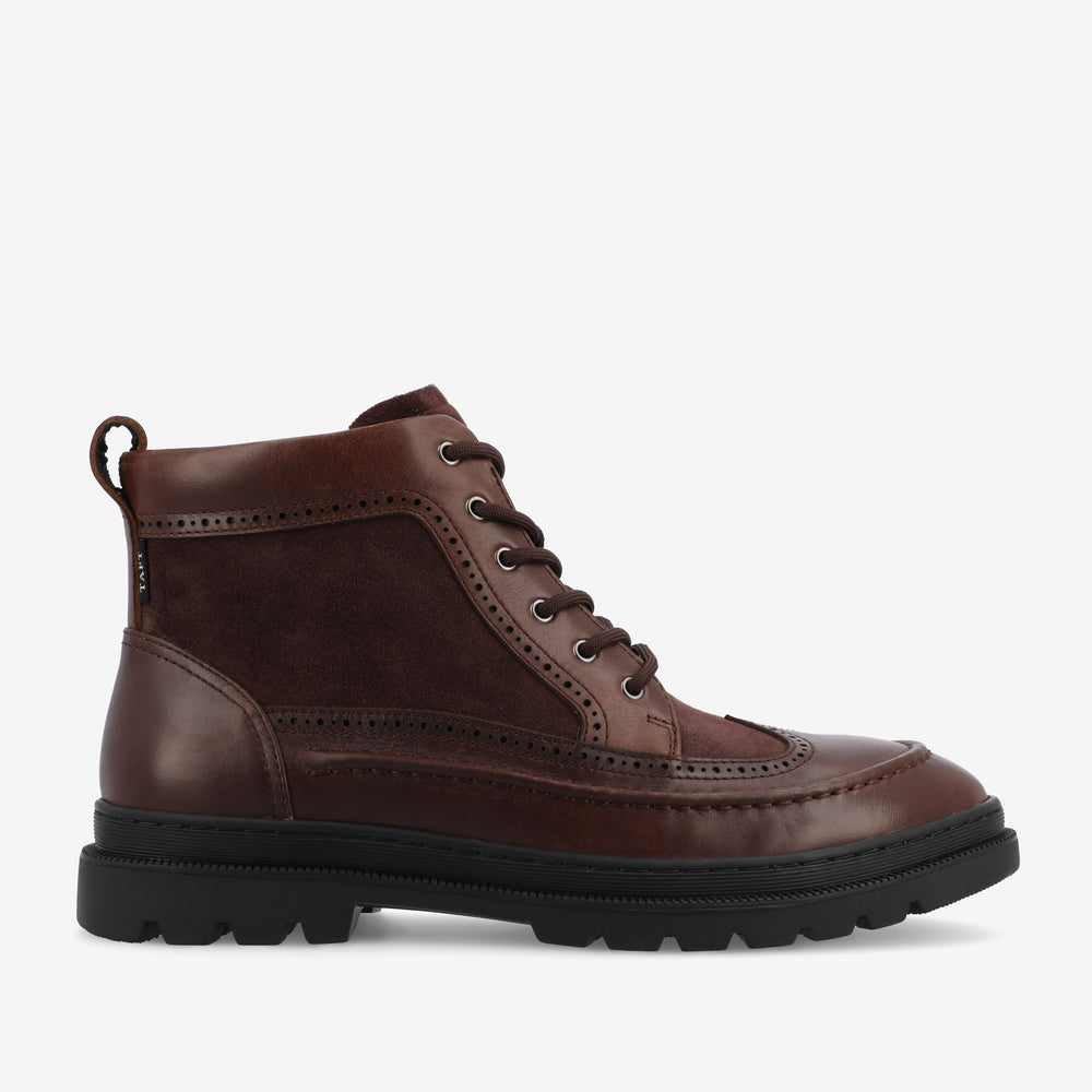 A brown leather and suede lace-up boot with a thick black rubber sole and pull-tab at the back on a white background.