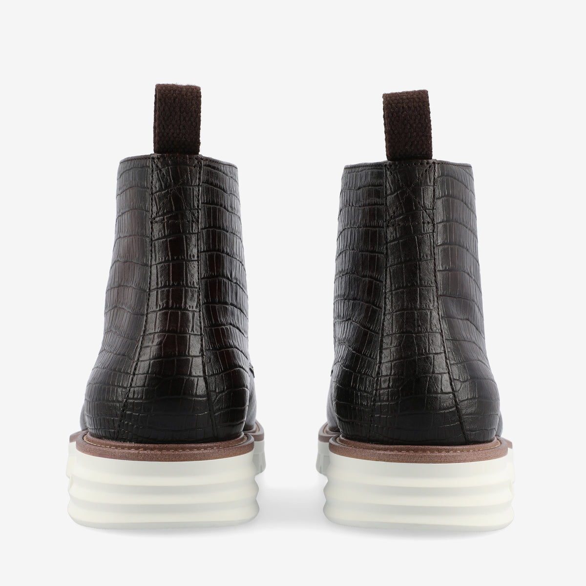 Rear view of a pair of dark brown, crocodile-textured ankle boots with white rubber soles and brown pull tabs.