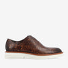 Side view of a brown, patterned leather dress shoe with white rubber sole and laces.