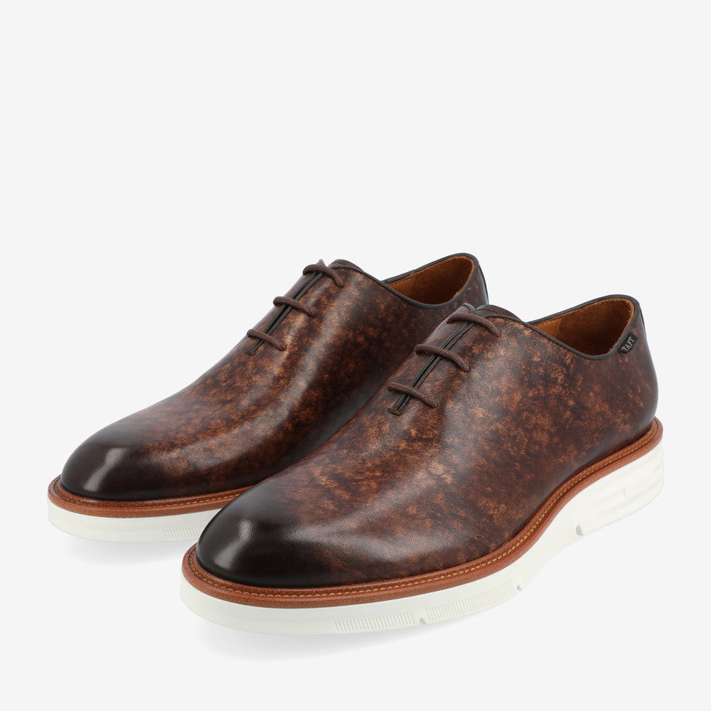 A pair of brown leather dress shoes with white rubber soles and laces placed side by side on a white background.