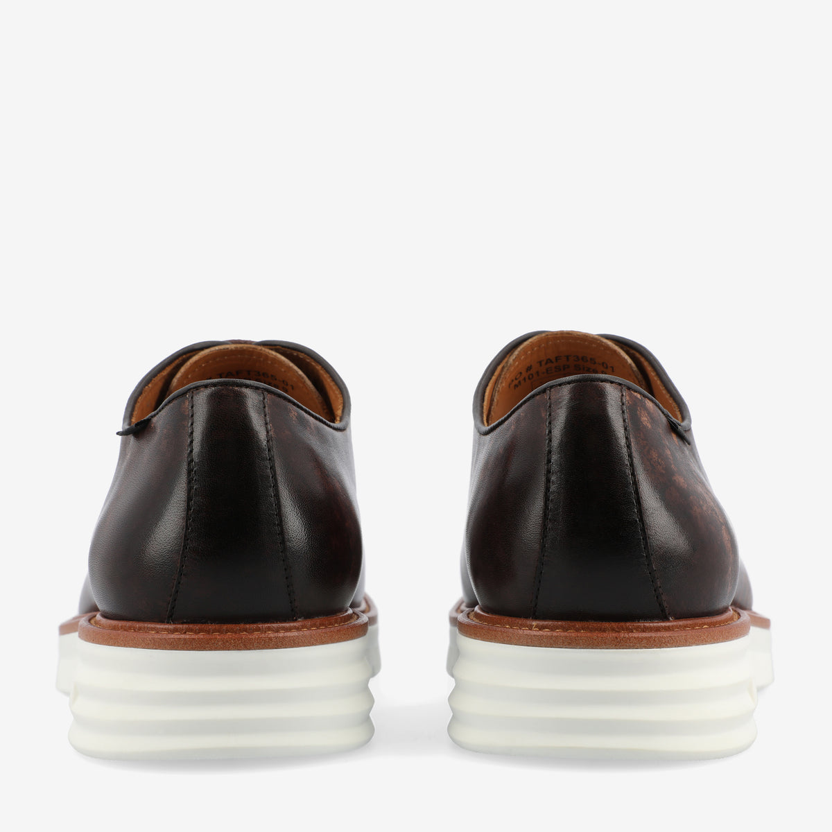 Rear view of a pair of brown leather dress shoes with white stacked rubber soles against a plain background.