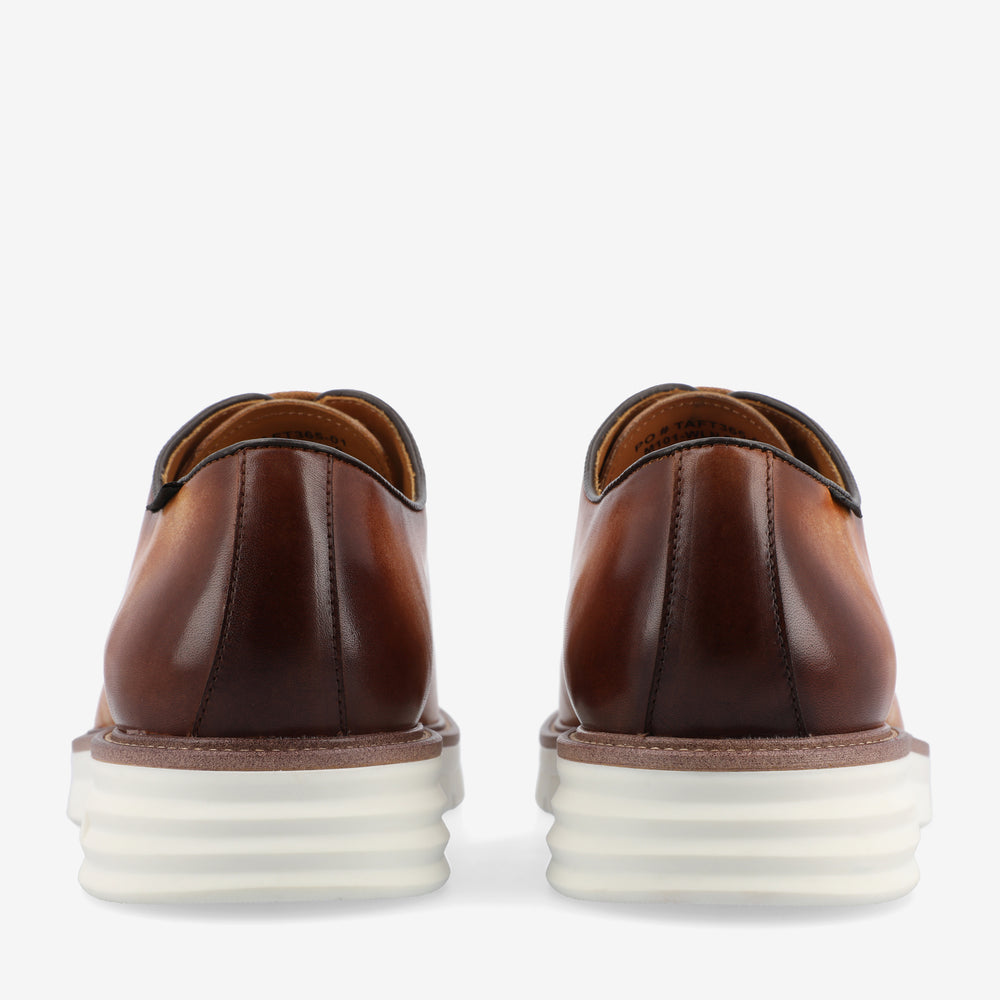 Rear view of a pair of brown leather shoes with white rubber soles, showing a sleek design and stitching details.