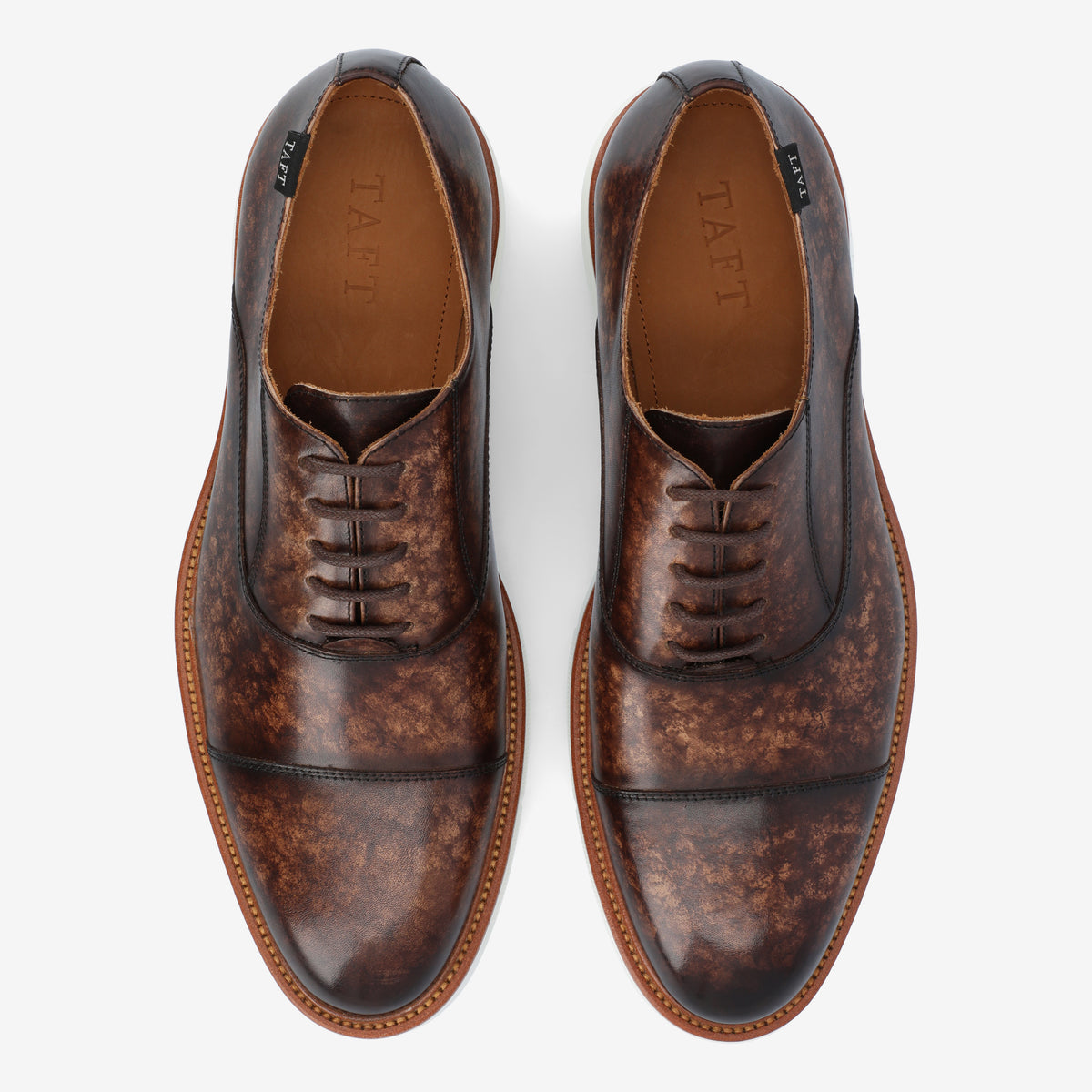 A pair of brown leather dress shoes with a mottled pattern, featuring laces and a brand name TAFT visible inside. The shoes are positioned side by side against a white background.