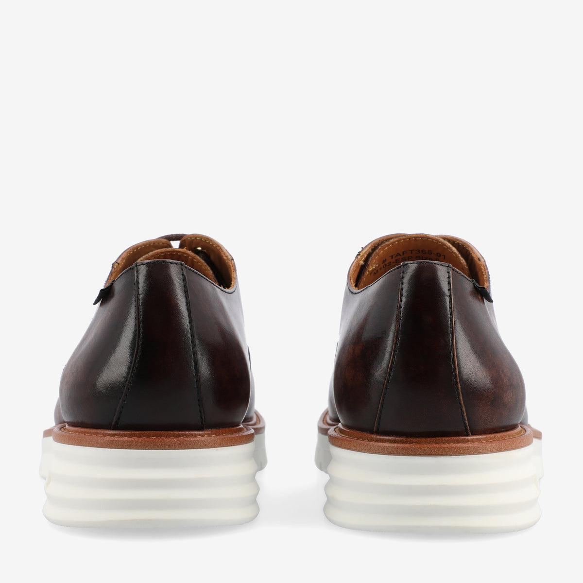 Rear view of a pair of brown leather dress shoes with white rubber soles.