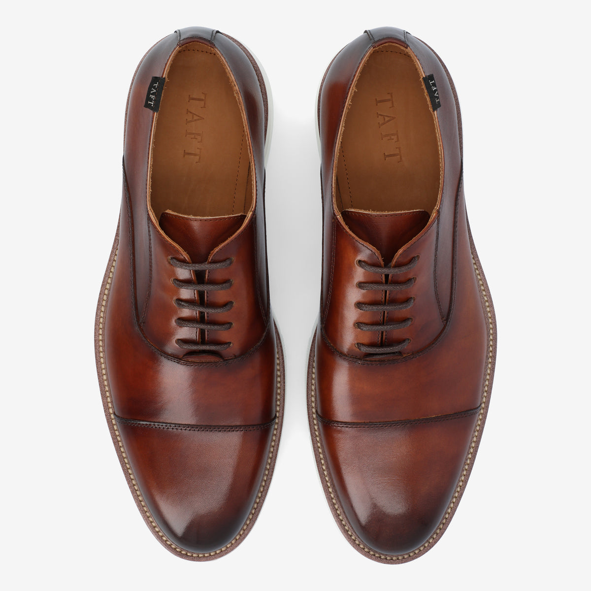 Top view of a pair of brown leather dress shoes with laces on a white background. The shoes have the brand name TAFT on the inner sole.