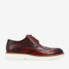 A side view of a red leather brogue shoe with decorative perforations, a white sole, and brown accents.