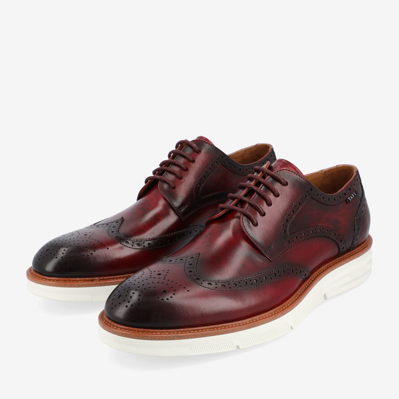 A pair of burgundy leather Oxford brogue shoes with white rubber soles and brown laces, featuring decorative perforations.