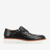 Black leather double monk strap shoe with silver buckles, brogue detailing, and a white rubber sole.