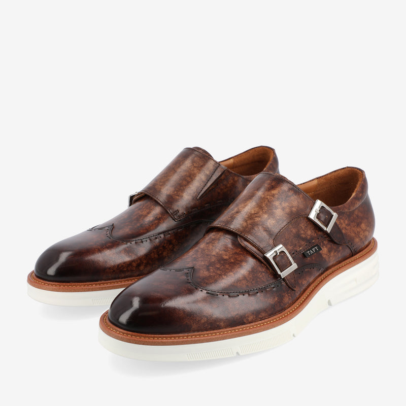 A pair of brown leather monk strap dress shoes with white soles, featuring two buckles on each shoe.