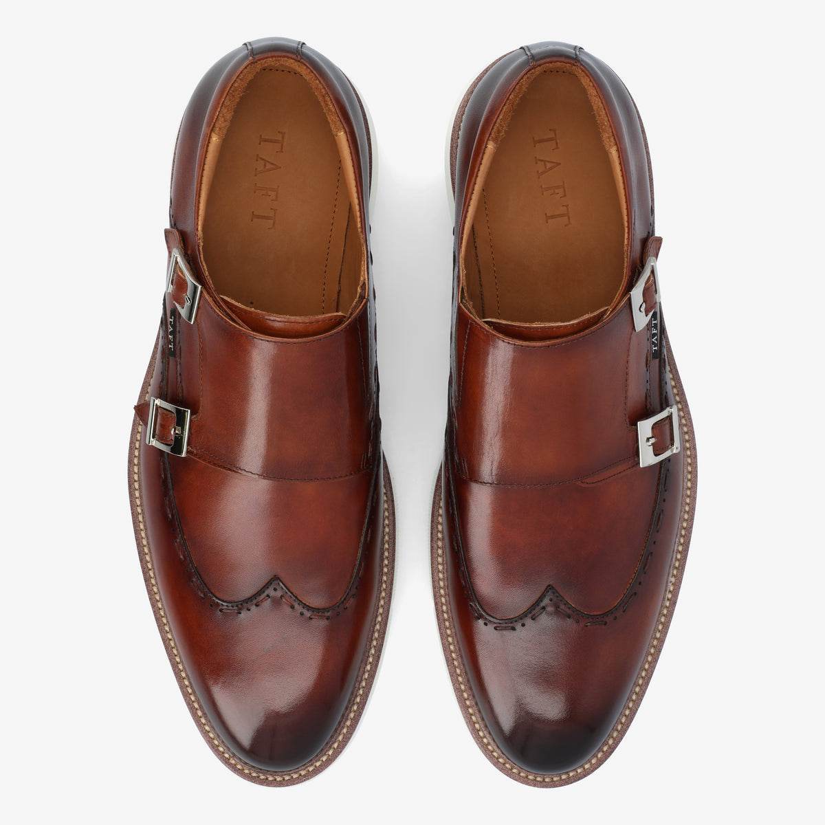 A pair of brown leather monk strap shoes with double buckles, featuring brogue detailing, viewed from above.