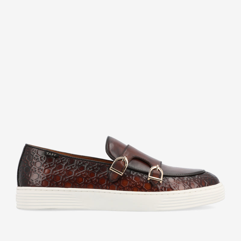 Dark brown leather slip-on shoe with a textured hexagonal pattern, two metallic buckles, and a white rubber sole, viewed from the side against a plain background.