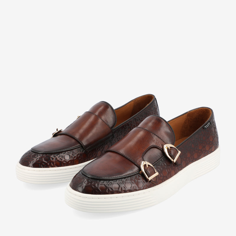 A pair of brown leather slip-on shoes with metal buckles and white rubber soles.