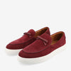 A pair of maroon suede slip-on shoes with white rubber soles and decorative bows on the top.