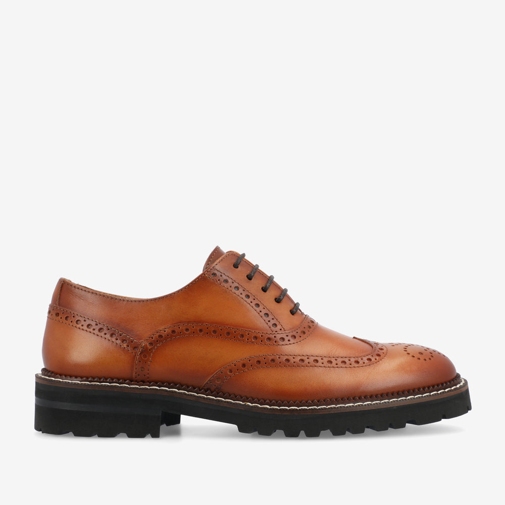 A brown leather brogue shoe with decorative perforations, black laces, and a thick black sole.