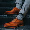 Person in gray pants and socks sitting, showing brown leather brogues with intricate detailing on metal stairs.