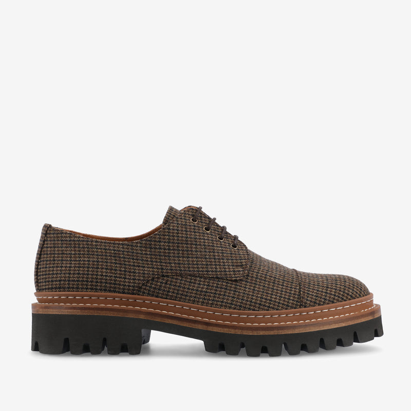 A single brown checkered lace-up shoe with a chunky black sole and white stitching detail on the side.