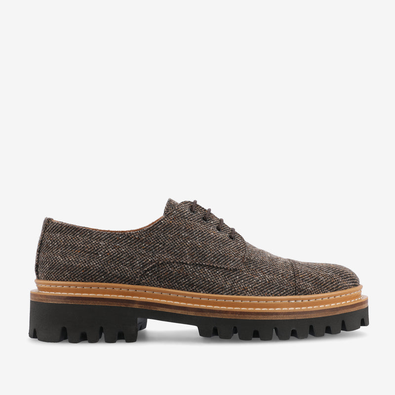 A brown tweed lace-up shoe with a thick, black rubber sole and tan leather midsole, displayed on a white background.