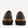 Rear view of a pair of brown tweed lace-up shoes with black chunky rubber soles.