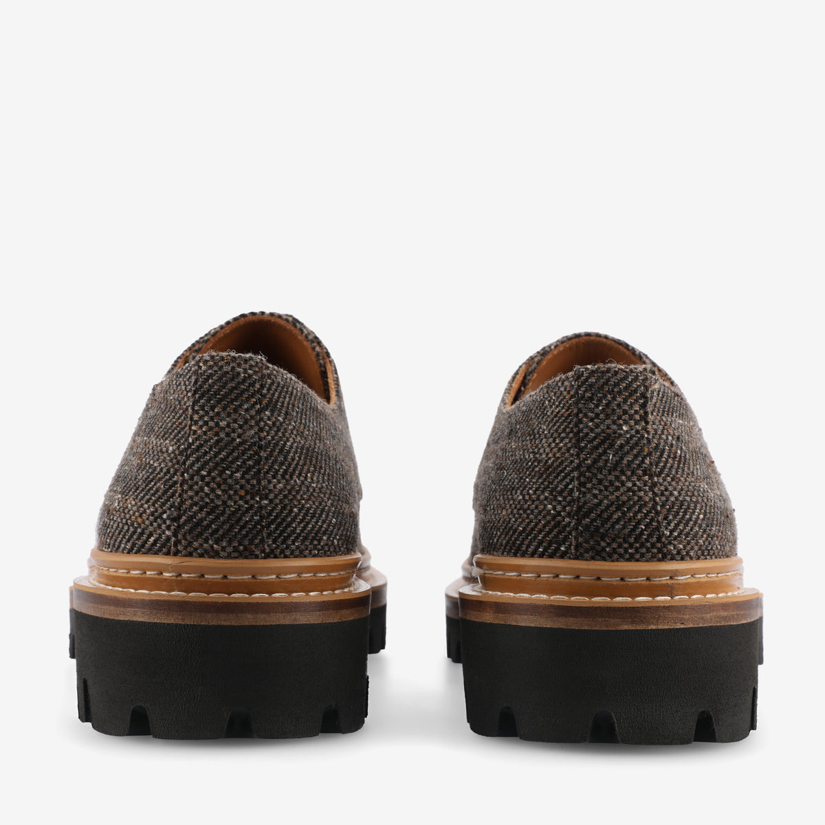 Rear view of a pair of brown tweed lace-up shoes with black chunky rubber soles.