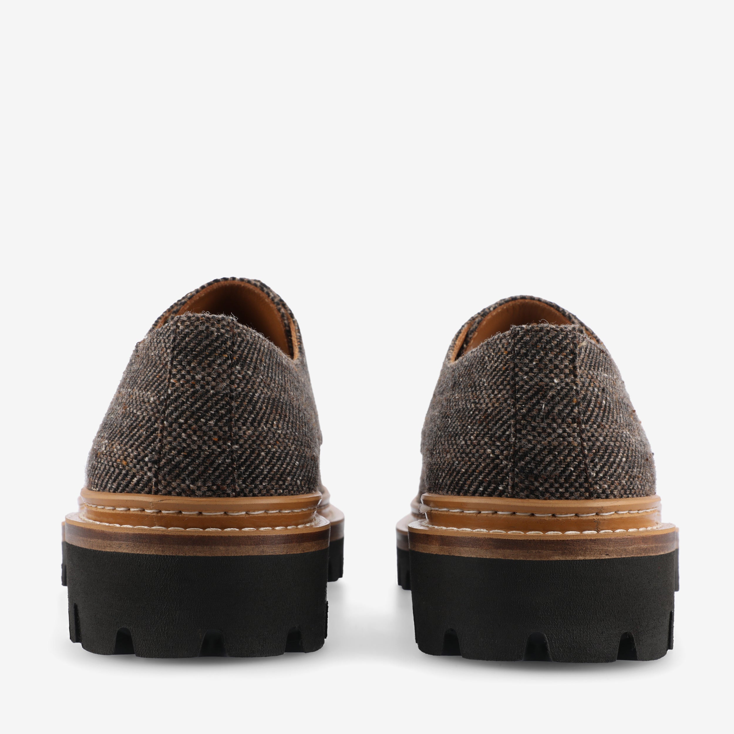 Rear view of a pair of brown tweed lace-up shoes with black chunky rubber soles.