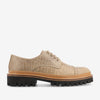 A beige textured lace-up shoe with a thick black sole and tan midsole, featuring a ridged pattern and detailed stitch work.