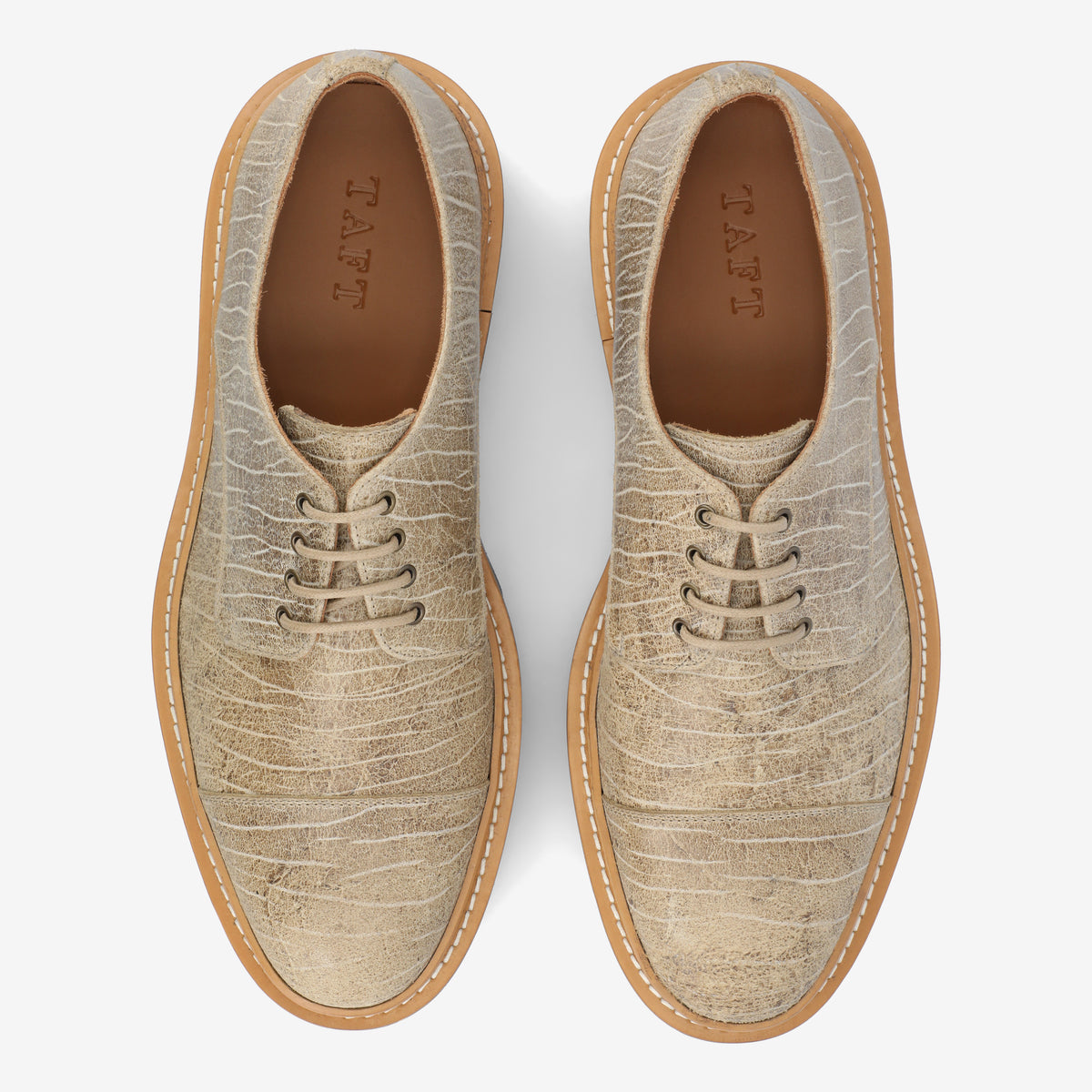 Top view of a pair of light beige textured leather shoes with laces and beige rubber soles, displaying the brand name TAFT inside.