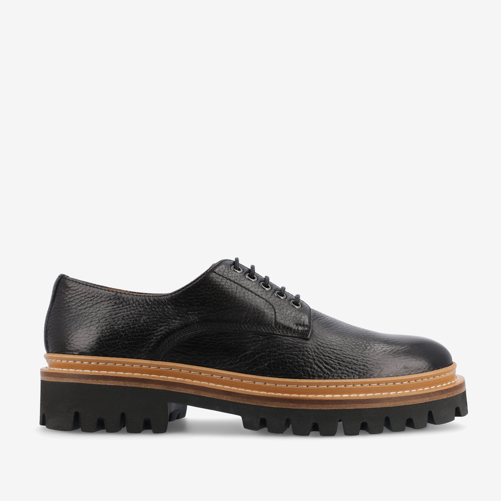 A black leather lace-up shoe with a thick, rugged tan and black sole.