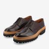 A pair of dark brown leather dress shoes with chunky soles and tan accents. The shoes have black laces and a textured, rugged appearance.