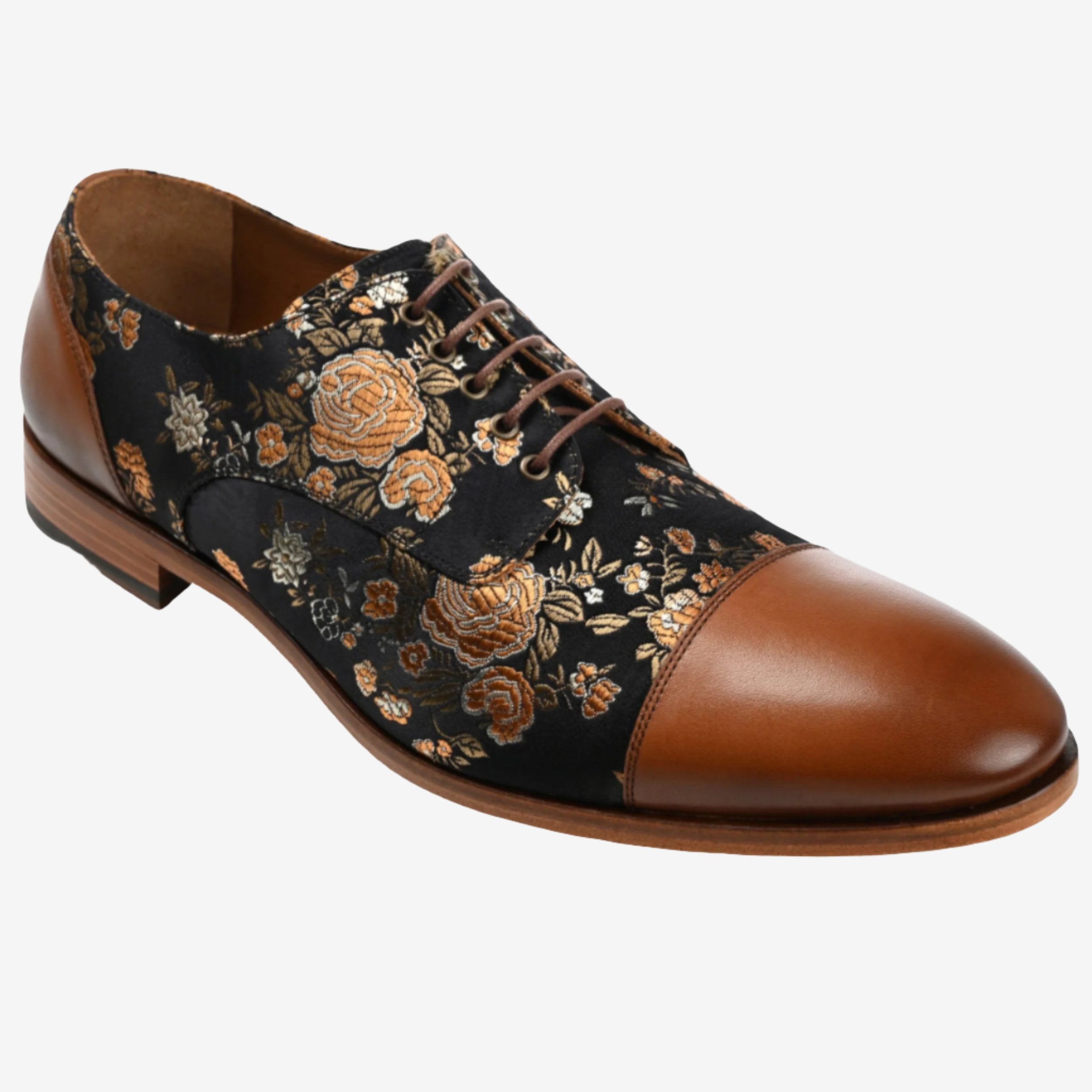 A men's dress shoe with a black floral-patterned fabric upper and brown leather accents, featuring a closed lacing system and brown sole.