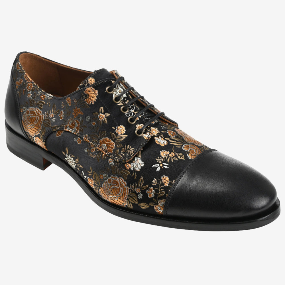 A black leather dress shoe with a floral pattern in gold and copper tones, featuring a closed lace-up design and a polished cap toe.