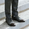 A person wearing gray dress pants and gray oxford shoes with dark brown toe caps is standing on a stone staircase.