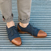 Person wearing rolled-up khaki pants and two-tone dress shoes with navy blue suede and brown leather cap toes, standing on a metal grate floor.