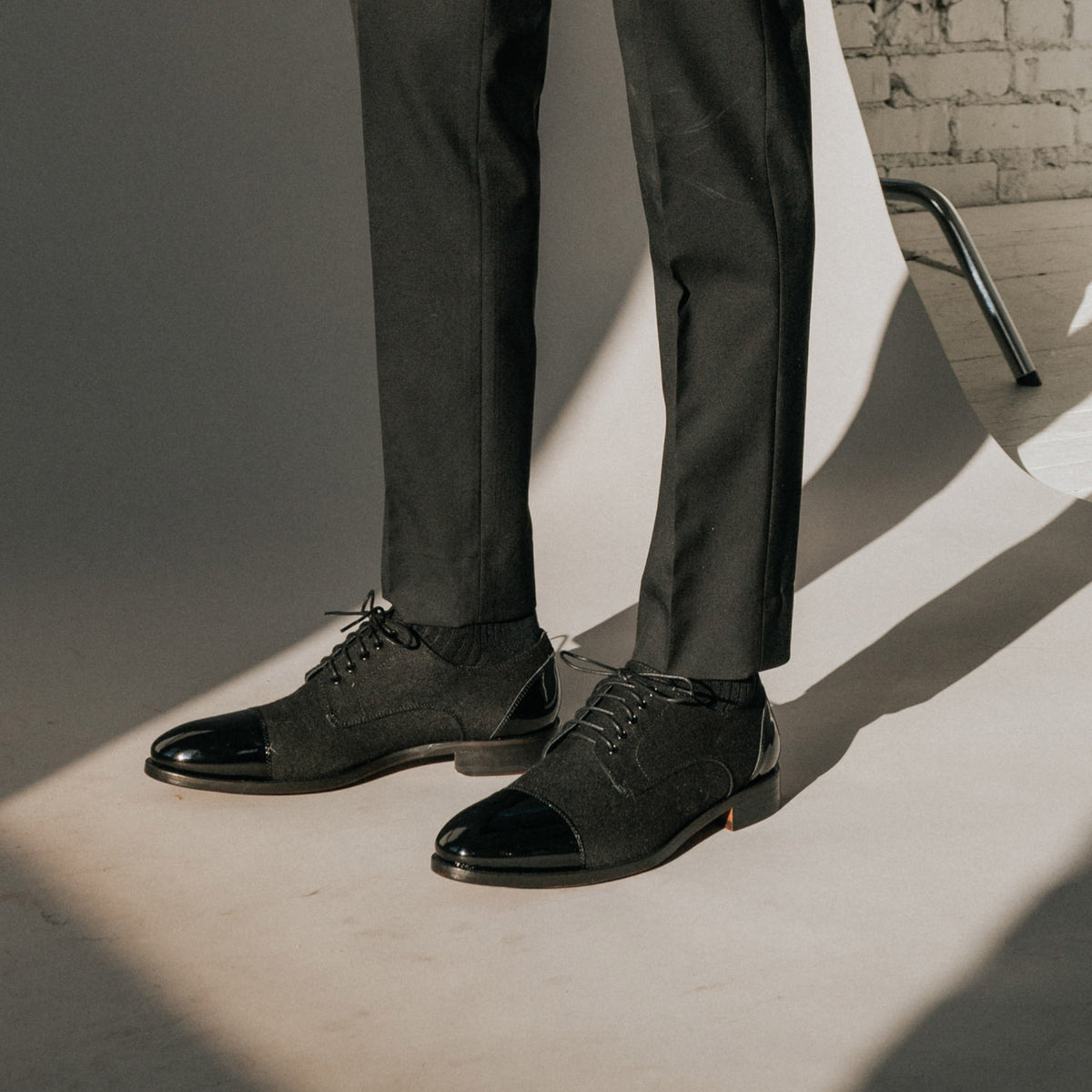 A person wearing black dress pants and black dress shoes stands on a light-colored floor with shadows cast by sunlight.