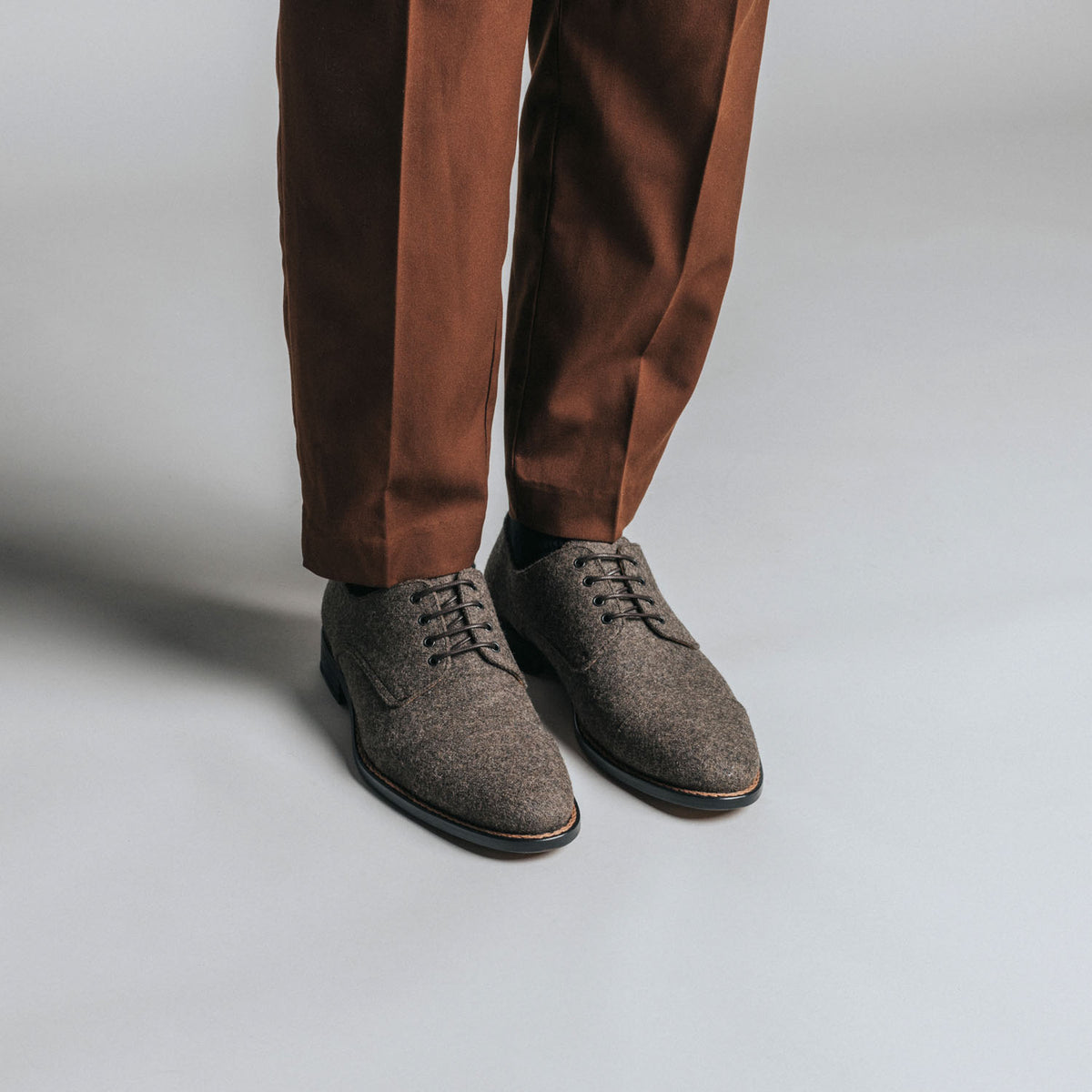 Person wearing brown pants and brown lace-up shoes standing on a light gray surface.