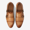 A pair of tan leather double monk strap shoes with embossed pattern and metal buckles.