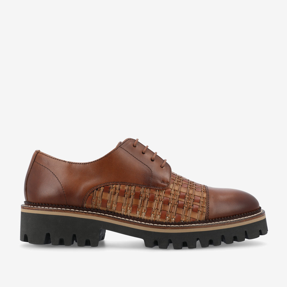 Brown leather oxford shoe with woven detailing on the sides, featuring black chunky soles with a beige accent stripe.