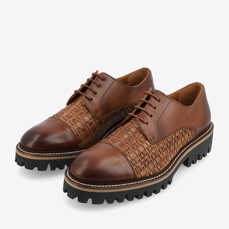 A pair of brown leather lace-up shoes with woven detailing on the sides and a thick, black rubber sole.