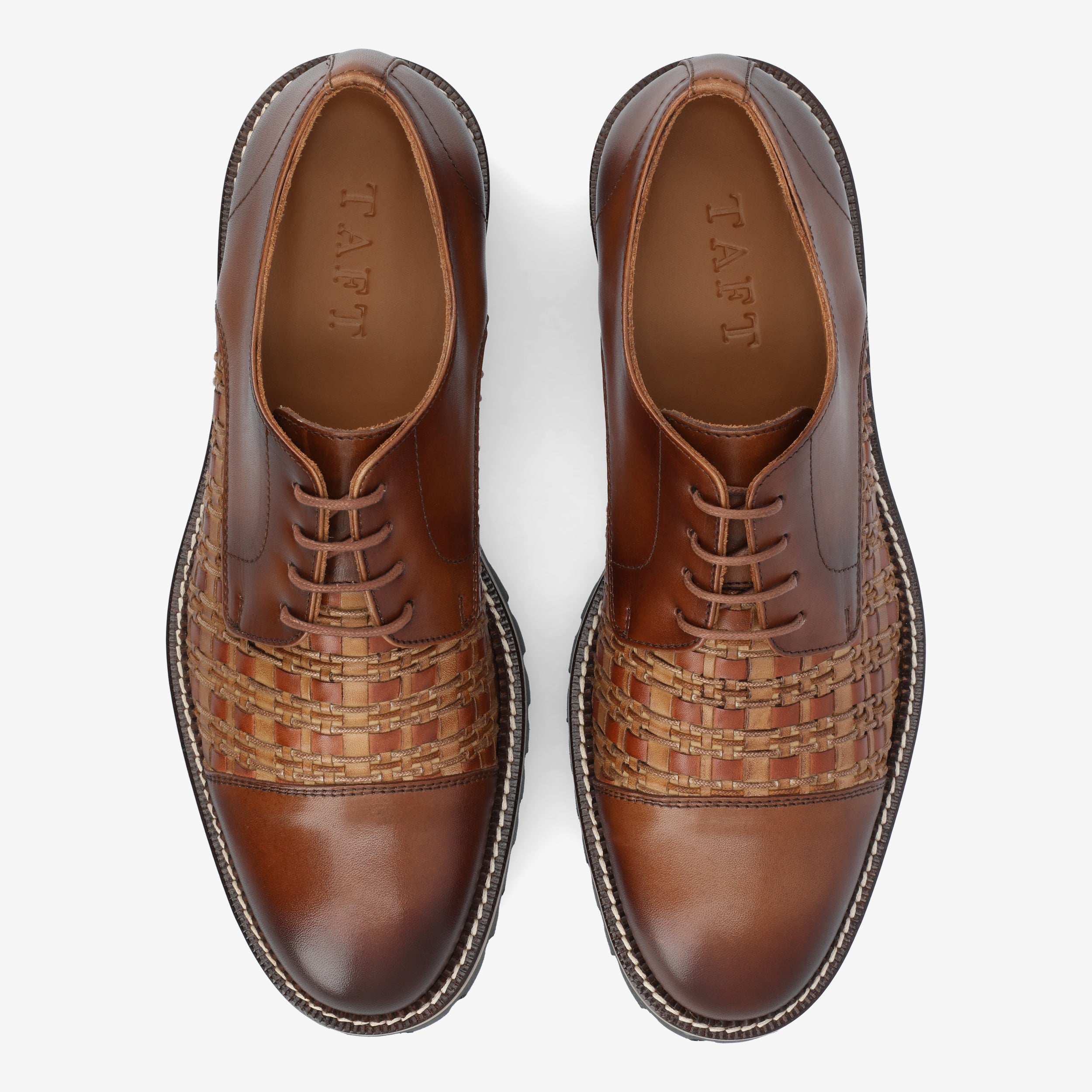 Top view of a pair of brown leather dress shoes with woven detailing across the midsection and TAFT embossed on the insoles.