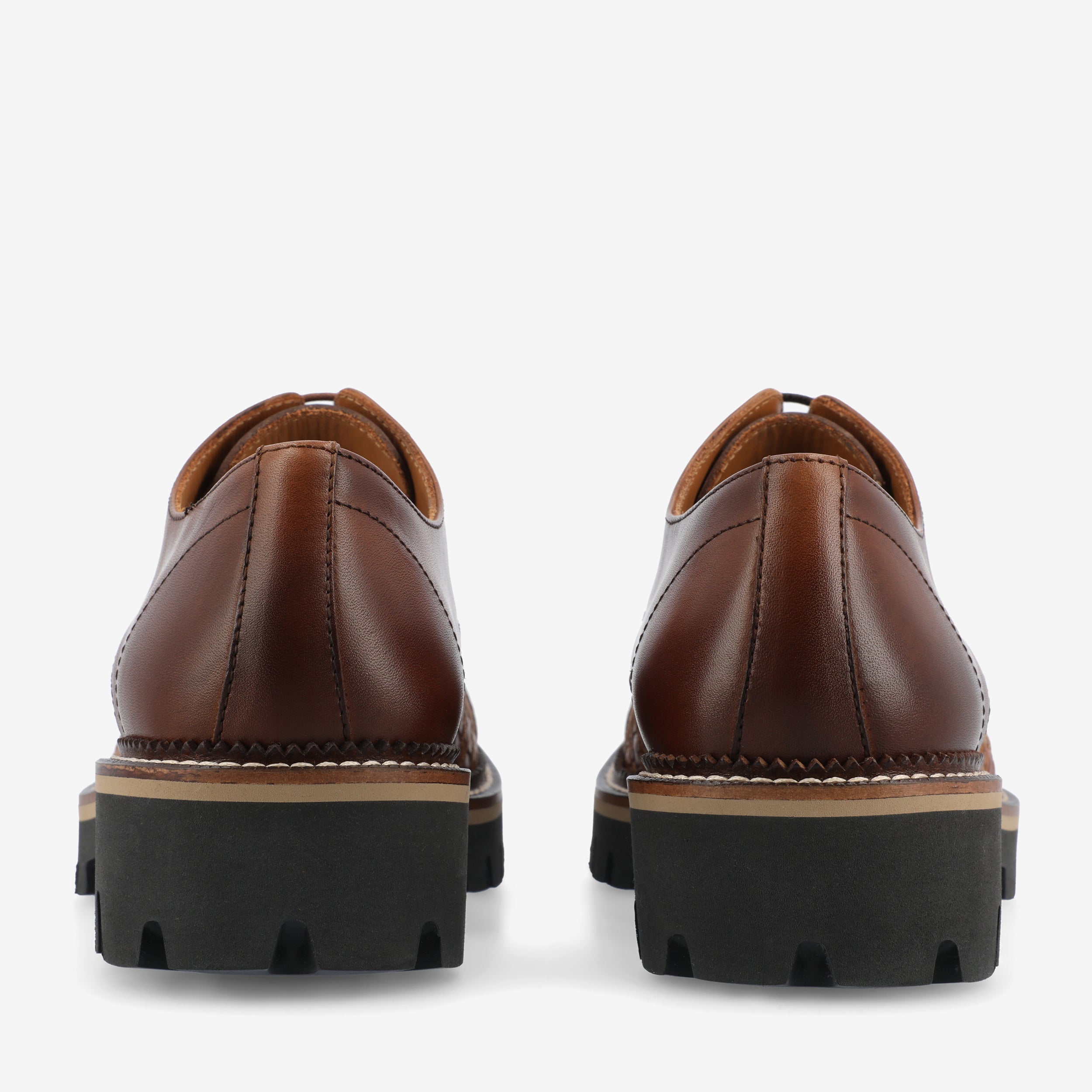 Rear view of a pair of brown leather shoes with black rubber soles featuring deep treads.