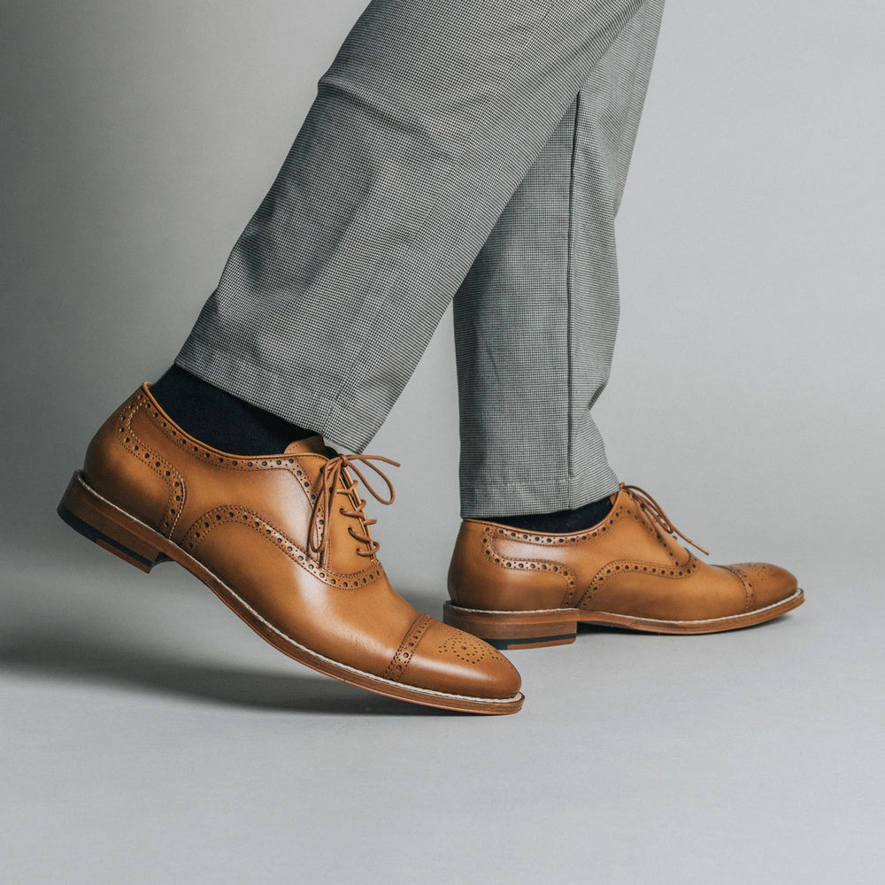 A person wearing gray dress pants and tan leather dress shoes stands against a neutral background.