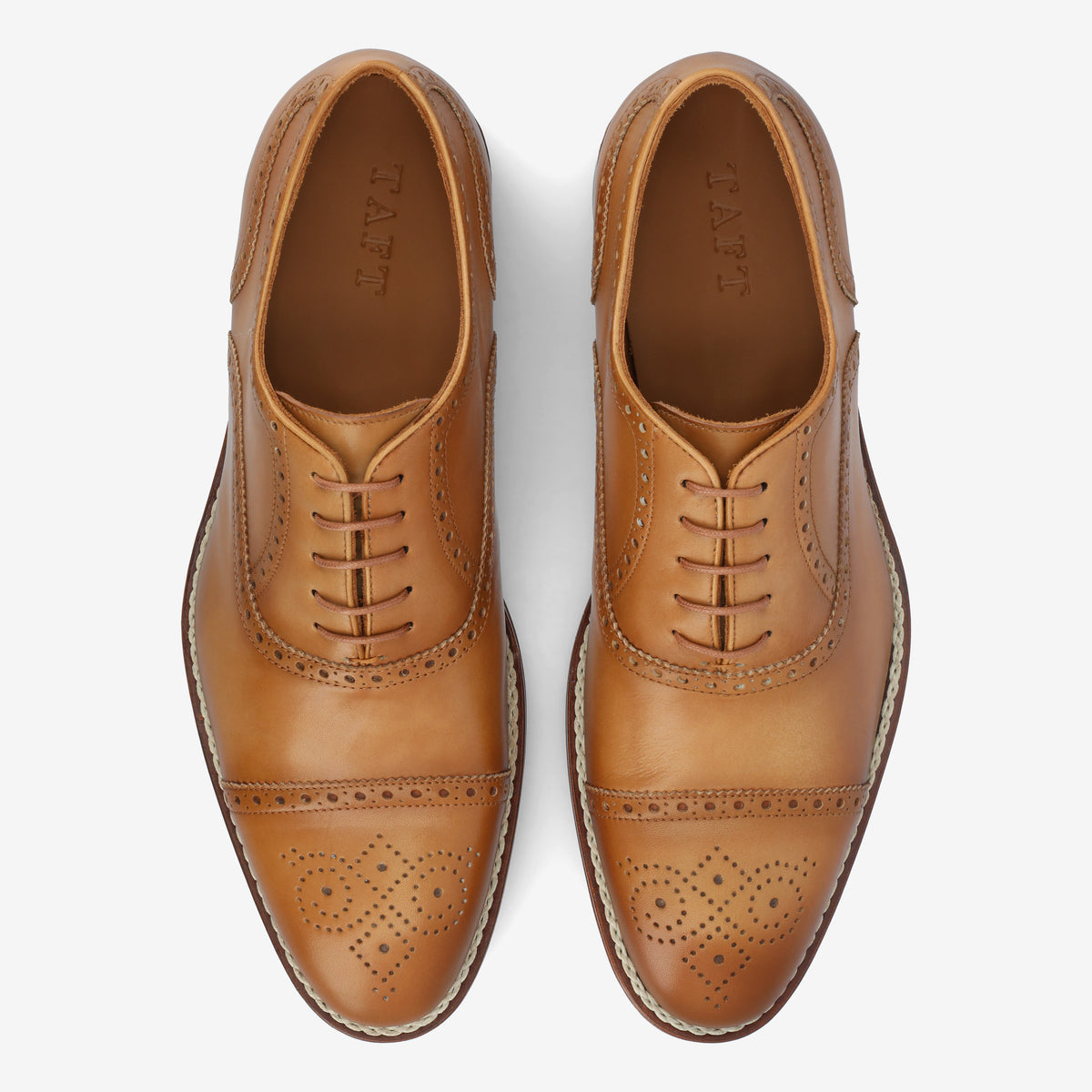 A pair of tan leather oxford brogue shoes with decorative perforations and closed lacing, viewed from above on a white background.