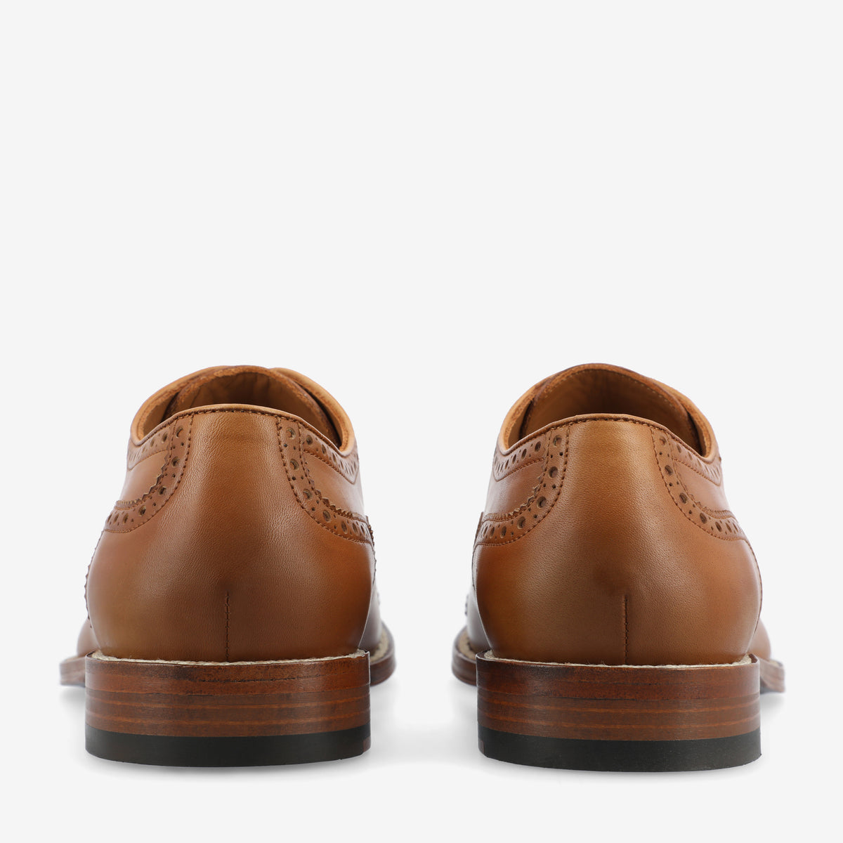 A back view of a pair of brown leather dress shoes with detailed brogue patterns and stacked wooden heels.