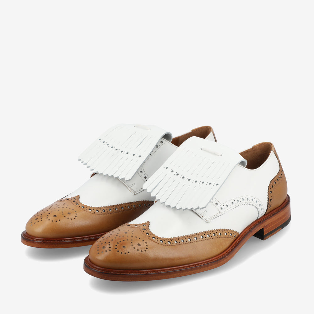 A pair of brown and white brogue shoes with fringe detailing on top, featuring intricate perforated patterns.